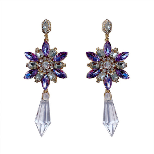 Pair of ornate earrings with purple and clear gemstones on a white background