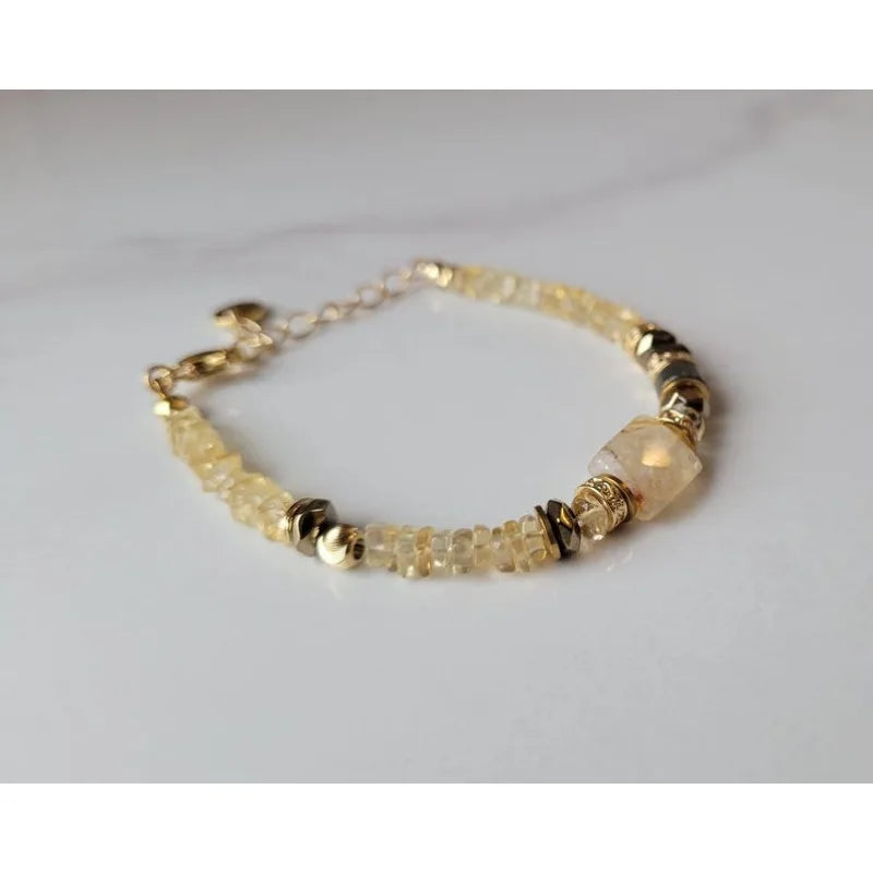 A delicate gold chain bracelet with small faceted pale yellow beads and a larger translucent pale yellow stone bead, displayed on a light gray surface.