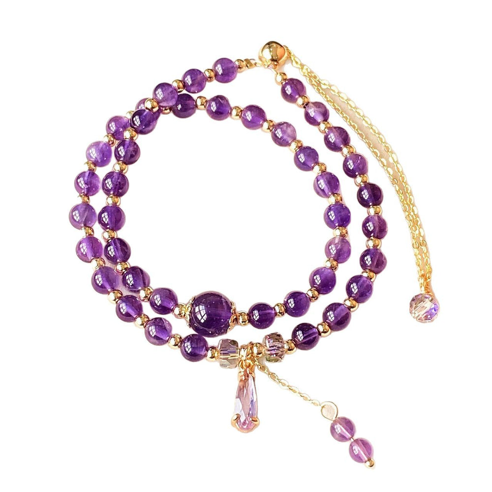 A double-strand amethyst bead mala necklace with gold-toned spacer beads, a large central amethyst crystal pendant, and a gold-toned chain extender with a small dangling amethyst bead on a white background.
