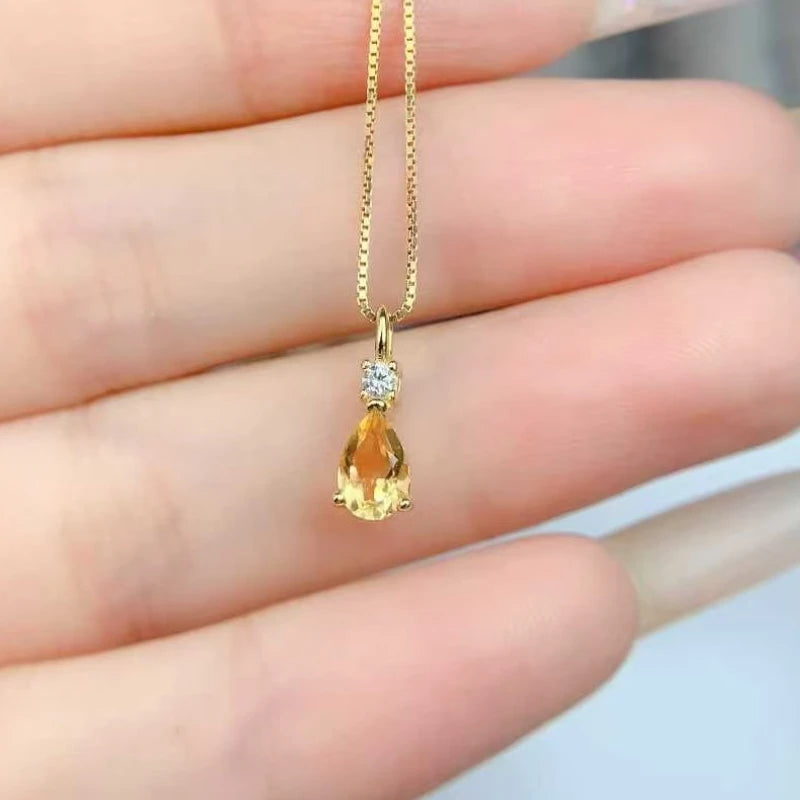 Gold necklace with a teardrop-shaped pendant held between fingers