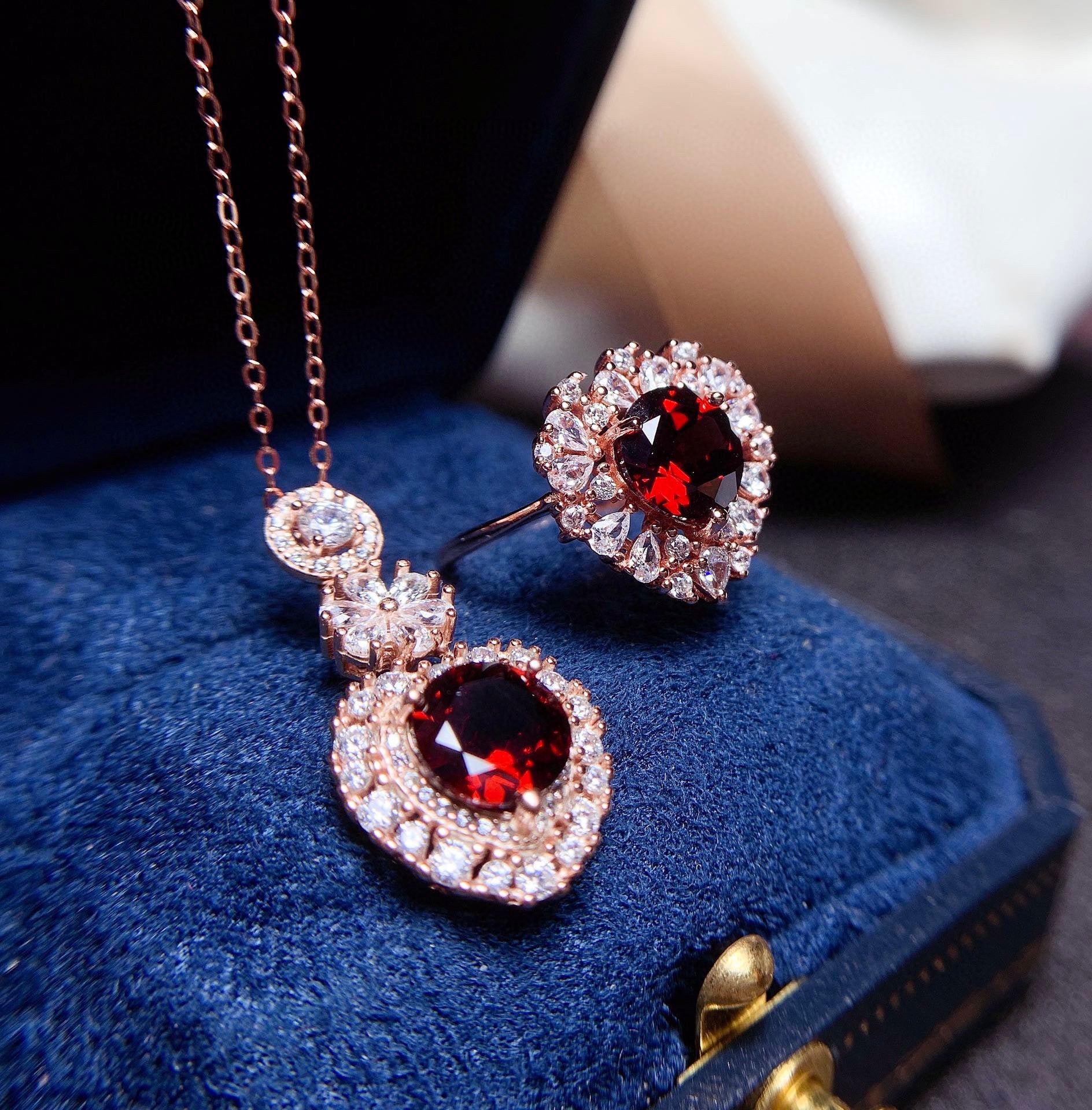 Jewelry set with red gemstones and rose gold accents on a blue cushion.