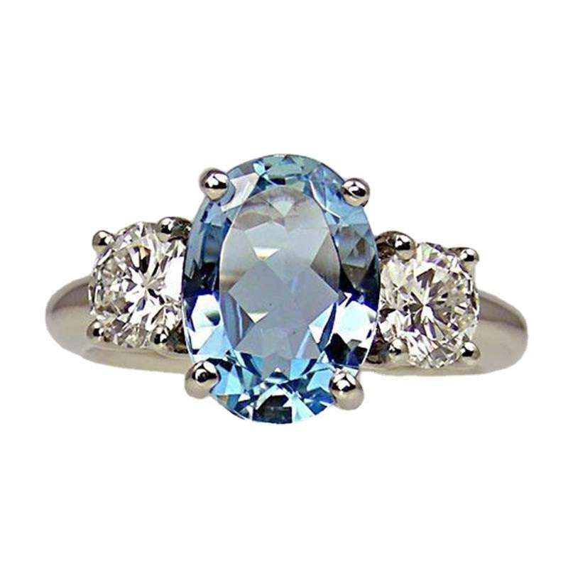 Ring with a central blue gemstone flanked by two smaller clear gemstones on a white background