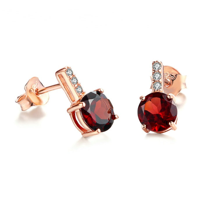 Rose gold earrings with red gemstones on a white background