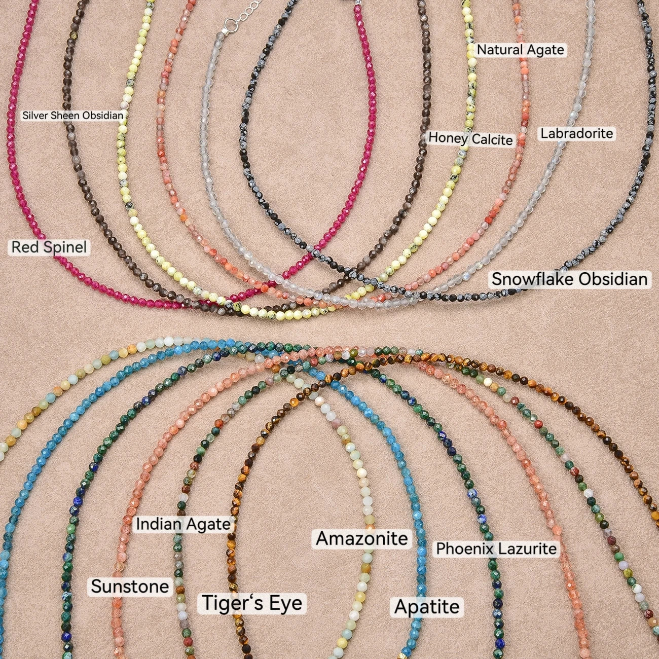A flat lay of multiple beaded necklaces arranged on a tan textured background, each labeled with its stone name such as Silver Sheen Obsidian, Red Spinel, Natural Agate, Honey Calcite, Labradorite, Snowflake Obsidian, Indian Agate, Amazonite, Phoenix Lazurite, Sunstone, Tiger's Eye, and Apatite.