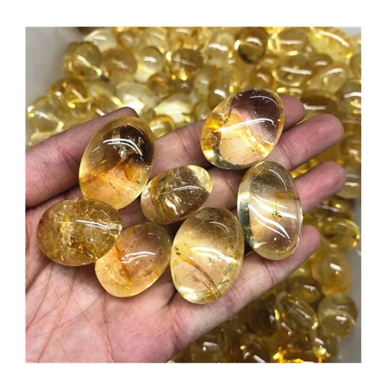 A hand holding several polished oval yellow gemstones, with more of the same stones piled in the background.
