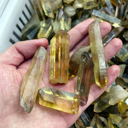 A hand holding several translucent yellow crystal points, with more similar crystals piled in the background.