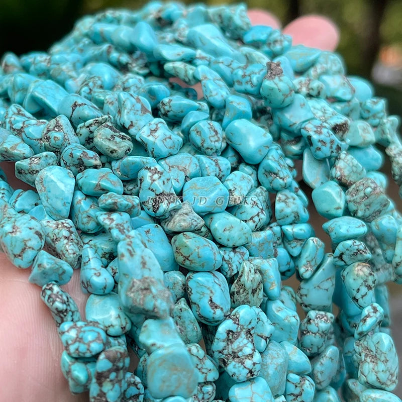 A close-up of a hand holding a pile of rough, polished turquoise stone chips with natural brown matrix veining.