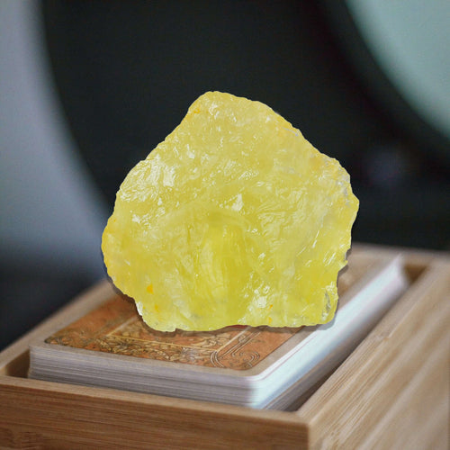 A raw, unpolished yellow crystal stone standing upright on top of a deck of playing cards inside a light wood tray.