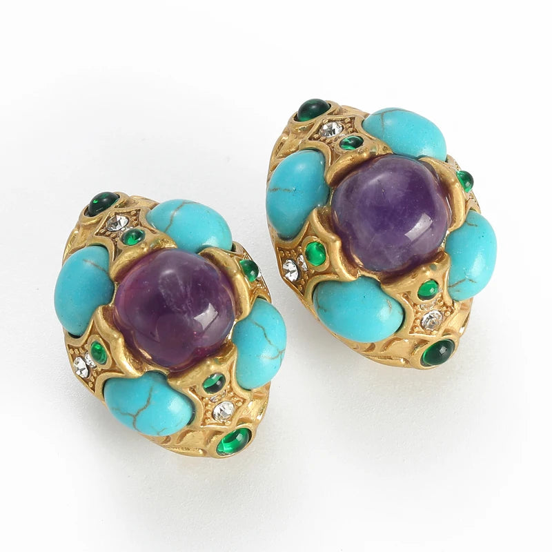 A pair of vintage gold-tone clip-on earrings featuring large oval purple amethyst centers, surrounded by turquoise-colored beads and small green and clear rhinestone accents, set against a plain white background.