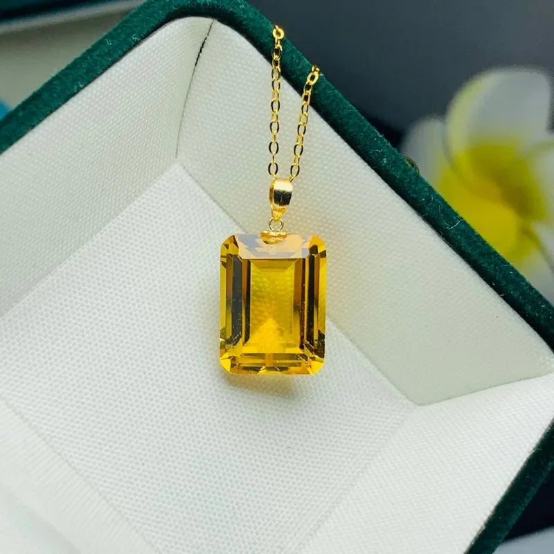 A yellow rectangular emerald-cut pendant necklace on a gold chain, resting inside a white-lined green jewelry box.